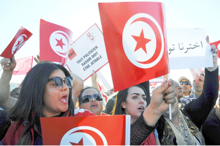 Tunisians with national flags show support for their government in front of the prime minister’s office in Tunis. Tunisian government froze the assets of eight businessmen suspected of corruption. — AP