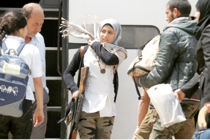 A rebel woman fighter fixes her head scarf as she carries her weapon before boarding a bus, as rebel fighters and their families evacuate the besieged Al-Waer district, after an agreement was reached between rebels and Syria›s army, in Homs, Syria, on Saturday.— Reuters