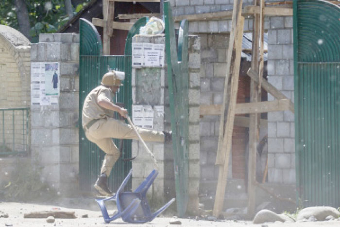 An Indian policeman kicks the gate of a college during a clash with Kashmiri students in Srinagar, Indian controlled Kashmir, on Tuesday. — AP