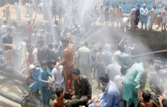 People cool off with water from water lines after they punctured them in protest against the power outages in their area in Karachi, Pakistan, on Tuesday. — Reuters