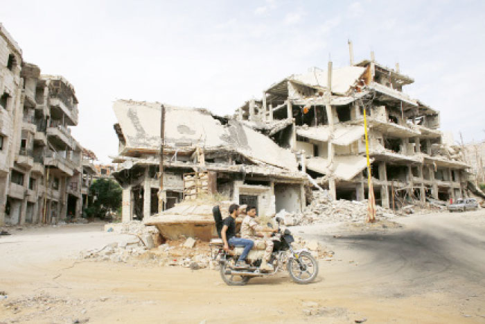 Syrians ride a motorcycle past destroyed buildings at the mountain resort town of Zabadani in the Damascus countryside. — AP