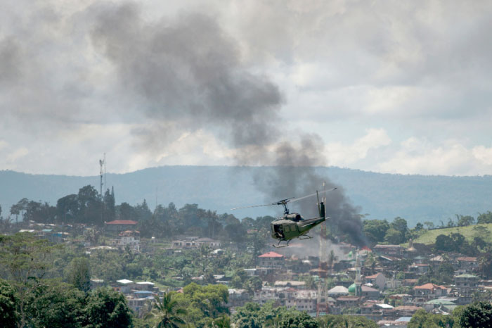 A helicopter flies through smoke billowing from houses after aerial bombings by Philippine Air Force planes on militant positions in Marawi on the southern island of Mindanao on Saturday. — AFP