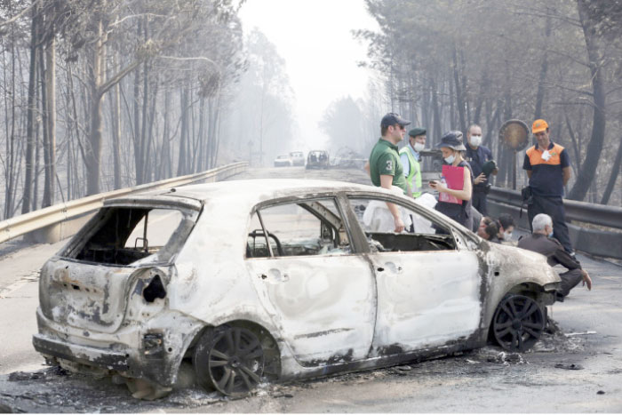 Police investigators stand by a burned car on the road between Castanheira de Pera and Figueiro dos Vinhos, central Portugal, on Sunday. — AP